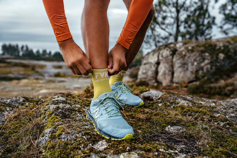 Man adjusting his green Fyke sock in a nature setting