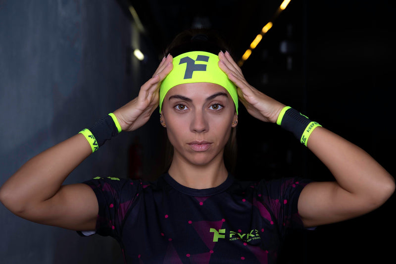 A woman wearing Fyke clothing and accessories adjusting her fluoroscent yellow headband with both hands.