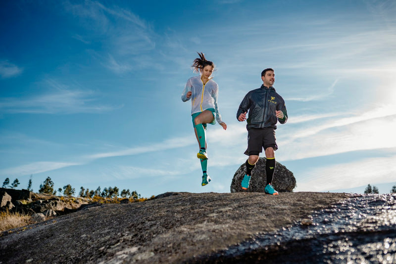 Man running and woman jumping in rocky area wearing Fyke sportswear.