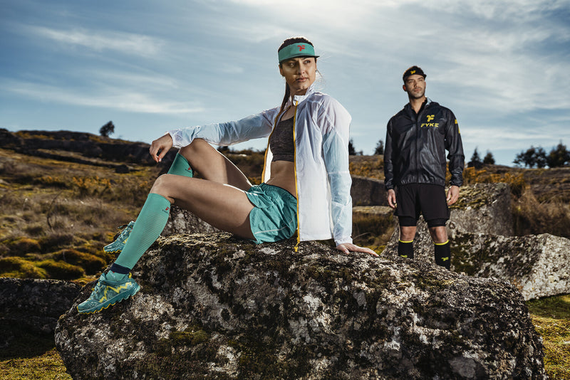 Woman sitting on a rock and man standing in a mountainous landscape wearing Fyke sportswear.