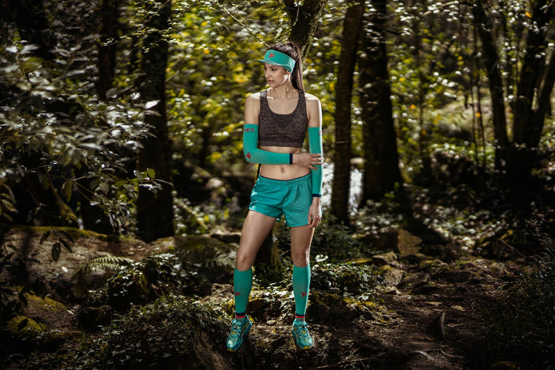 Runner with arm sleeves and other turquoise sports accessories in the middle of a forest.