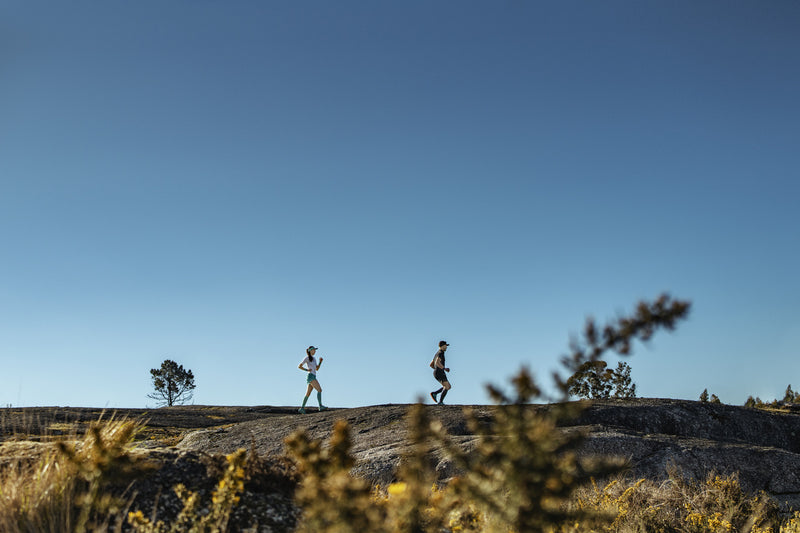 Man and woman running in a rocky landscape wearing running clothing.