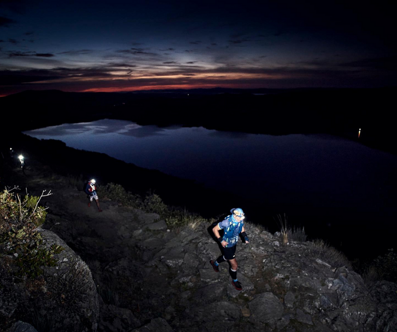 Runners in a night trail running race with a beautiful landscape of a lake.