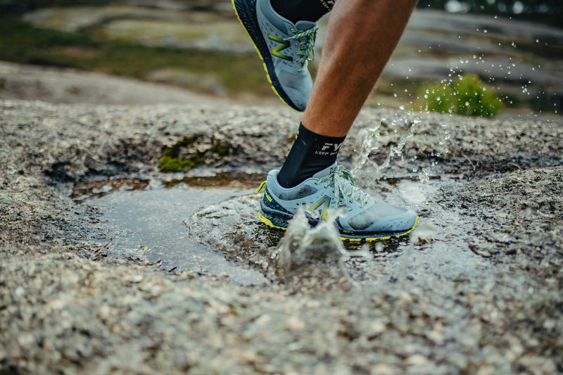 Man's leg running on rocky ground stepping in puddle of water splashing it.