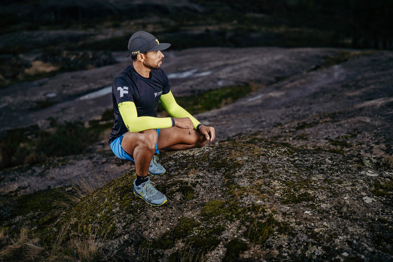 A man wearing Fyke trail running hat and clothing nestled in rocky terrain.