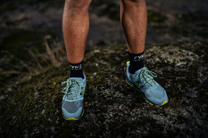 Man's legs on a rock wearing Fyke sports compression socks and a pair of sneakers.