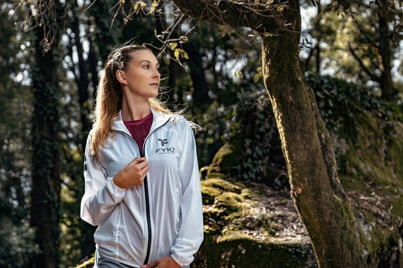 Woman in a forest environment wearing a Fyke waterproof running jacket.