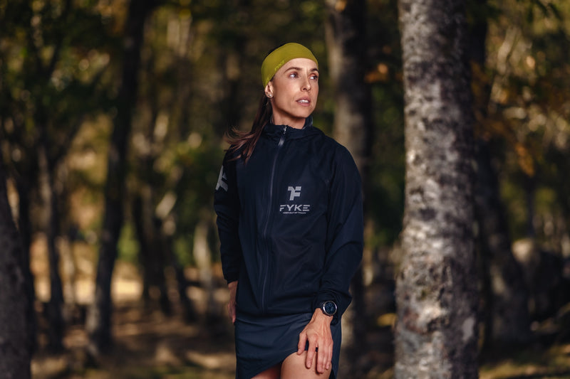 Woman in the forest wearing a black Fyke winter running jacket.