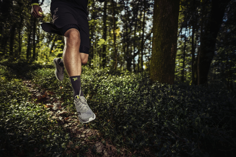 Man jumping in the middle of a trail in a forest area with Fyke sports equipment.