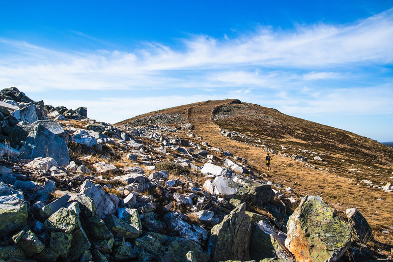 Athlete running on mountain trail near rocky terrain